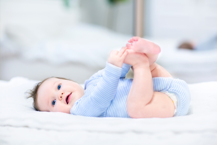 Sweet little baby playing with her feet next to a mirror in a white bedroom
