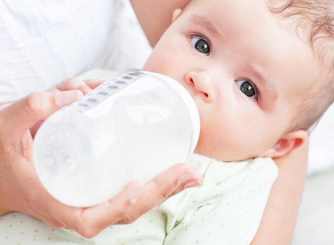 Close-up of a baby drinking milk in his mother's arms at home