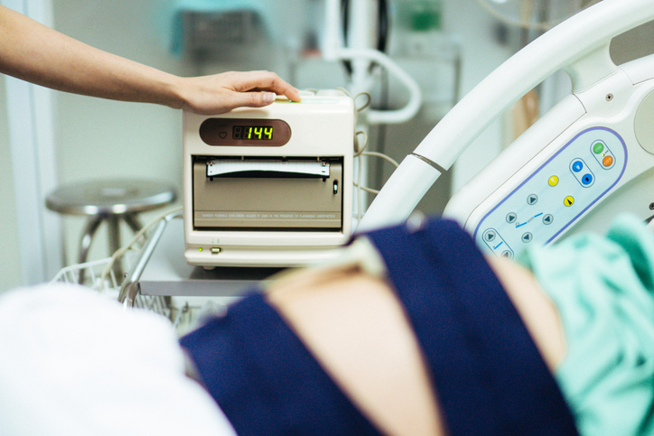 Doctor examining belly of expectant mother in hospital room. Thailand.