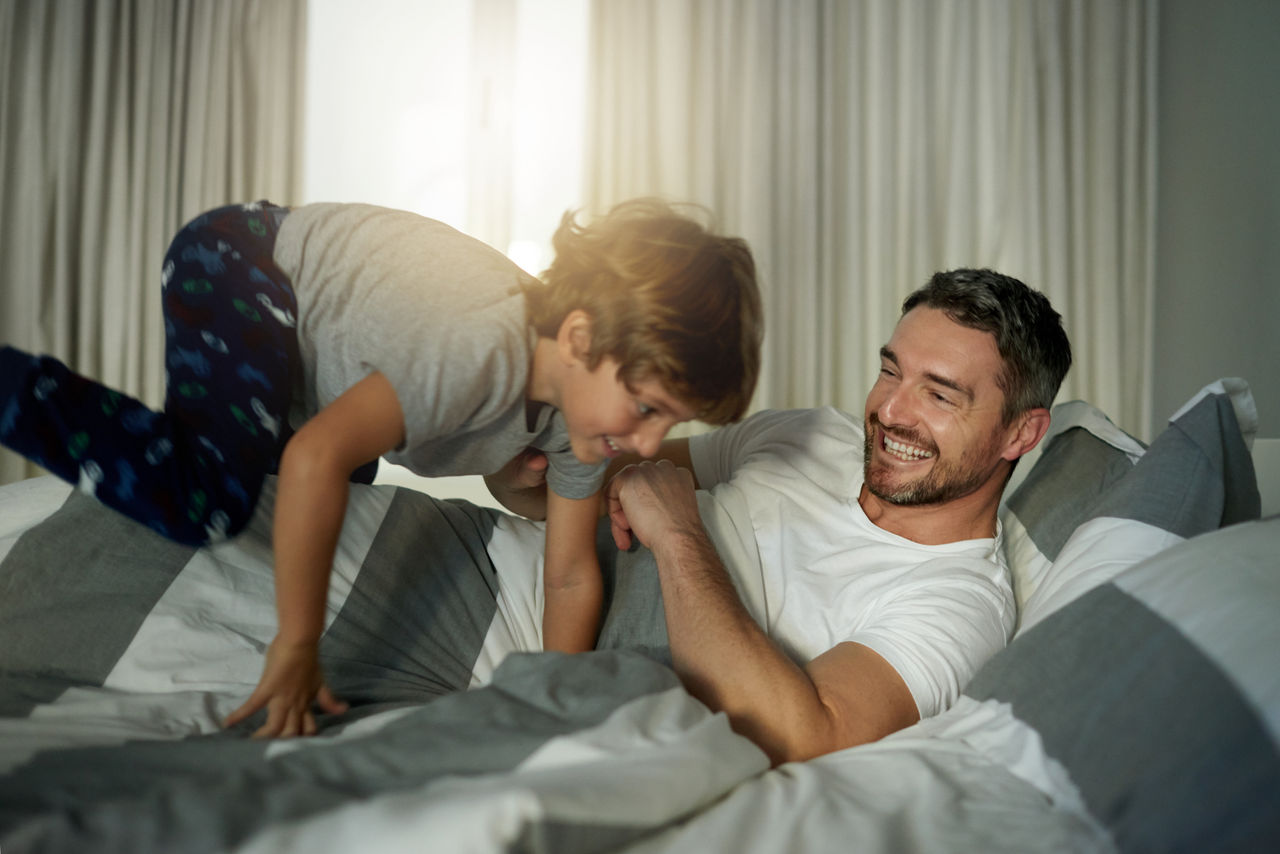Shot of a cute little boy jumping on his fatherâ  s bed in the morning