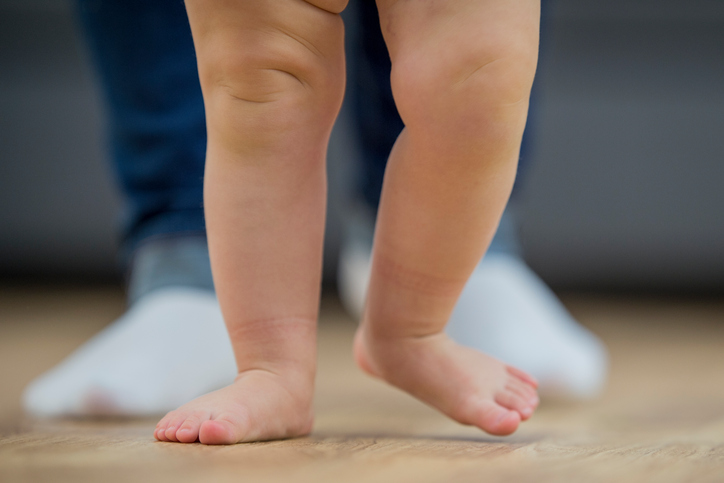 A baby takes her first steps.They are in a cozy living room on hardwood flooring.