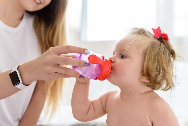 Enjoying motherhood. Happy young woman is giving small bottle of water to her little child. She is holding it near her mother and smiling