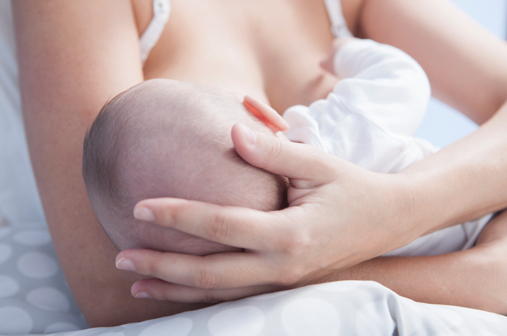 Mother holds her baby head while he is breastfed. Closeup