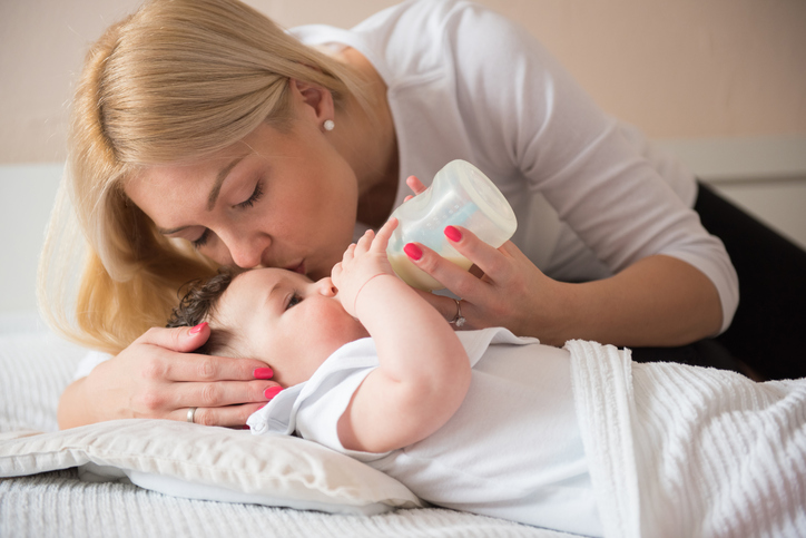 Single mother lying down with baby boy, feeding him and kissing in a forehead